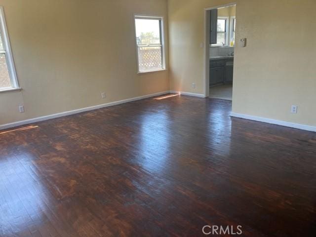 unfurnished room with baseboards, plenty of natural light, and dark wood-style floors