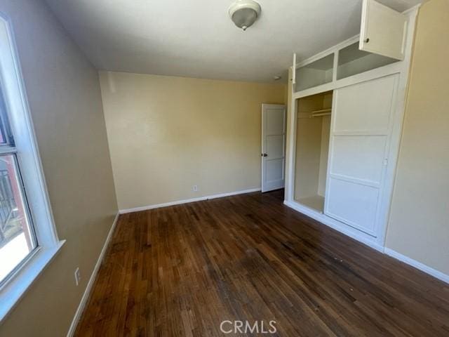 unfurnished bedroom with dark wood finished floors, a closet, and baseboards