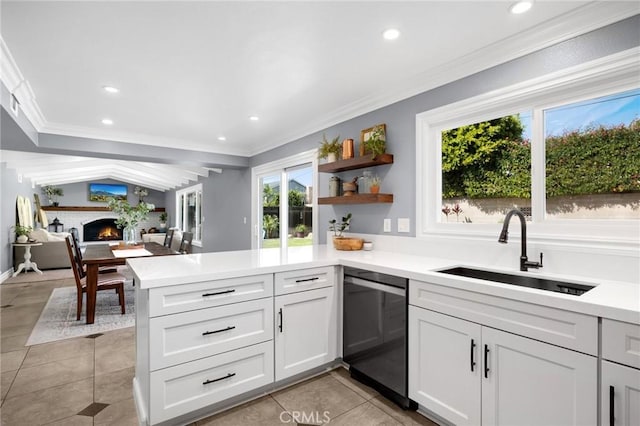 kitchen featuring a peninsula, a warm lit fireplace, a sink, light countertops, and dishwasher