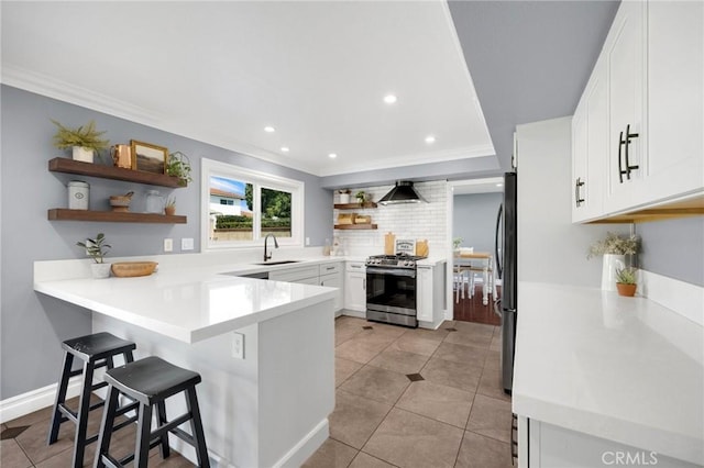 kitchen with open shelves, a peninsula, a sink, stainless steel gas range oven, and wall chimney exhaust hood