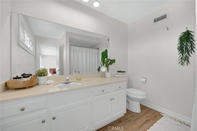 bathroom with vanity, wood finished floors, visible vents, baseboards, and toilet