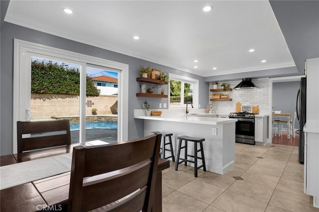 kitchen with open shelves, a peninsula, crown molding, decorative backsplash, and stainless steel range with gas stovetop