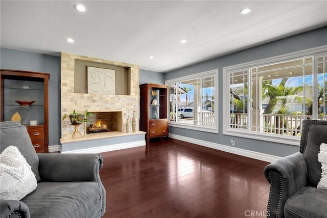 living area featuring a stone fireplace, recessed lighting, wood finished floors, and baseboards