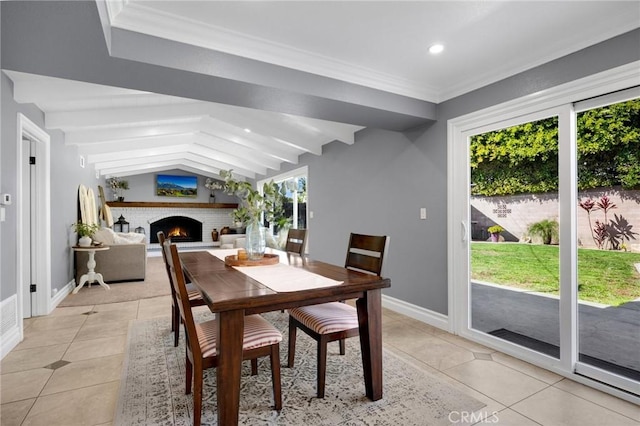 dining space featuring light tile patterned floors, baseboards, lofted ceiling with beams, a fireplace, and crown molding