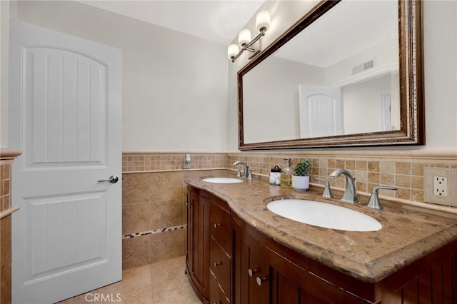 bathroom featuring a sink, visible vents, tile walls, and a wainscoted wall