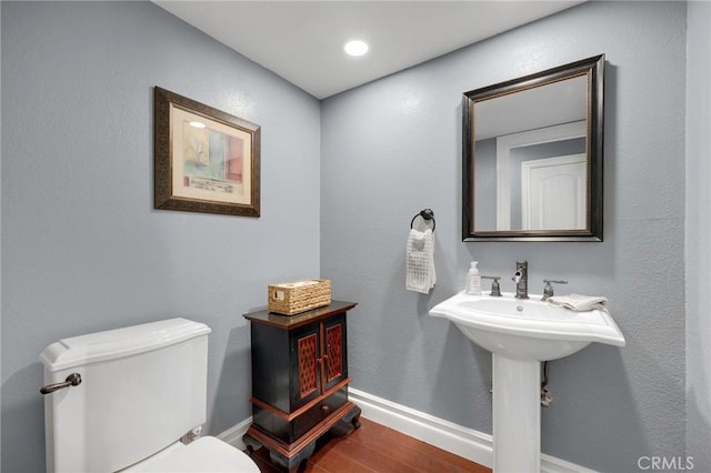 bathroom with toilet, wood finished floors, baseboards, and a sink