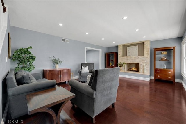 living area featuring visible vents, baseboards, recessed lighting, a stone fireplace, and dark wood-type flooring