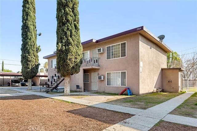 view of front of house with stucco siding, stairs, and a wall mounted AC