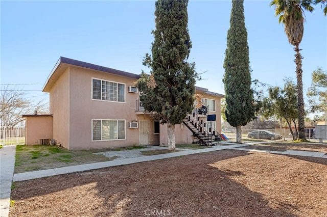 view of property with a wall mounted air conditioner, stairway, stucco siding, and fence