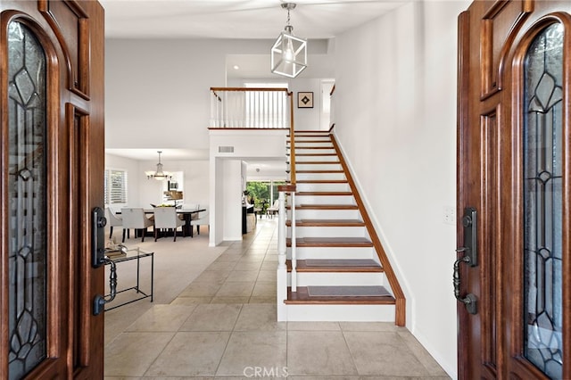 entryway with visible vents, stairway, light tile patterned floors, baseboards, and a towering ceiling