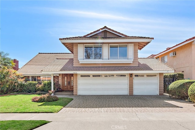 traditional-style house with a tile roof, decorative driveway, a front lawn, and an attached garage