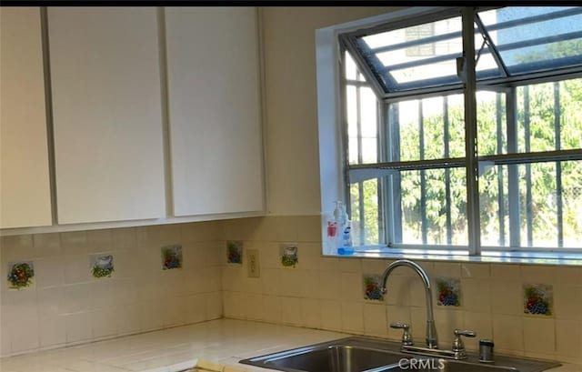 kitchen featuring tasteful backsplash, white cabinets, a healthy amount of sunlight, and a sink