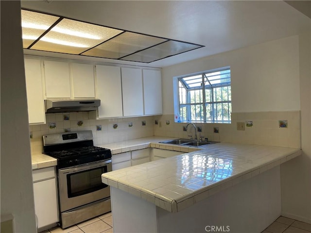 kitchen with under cabinet range hood, tile countertops, a peninsula, gas stove, and a sink