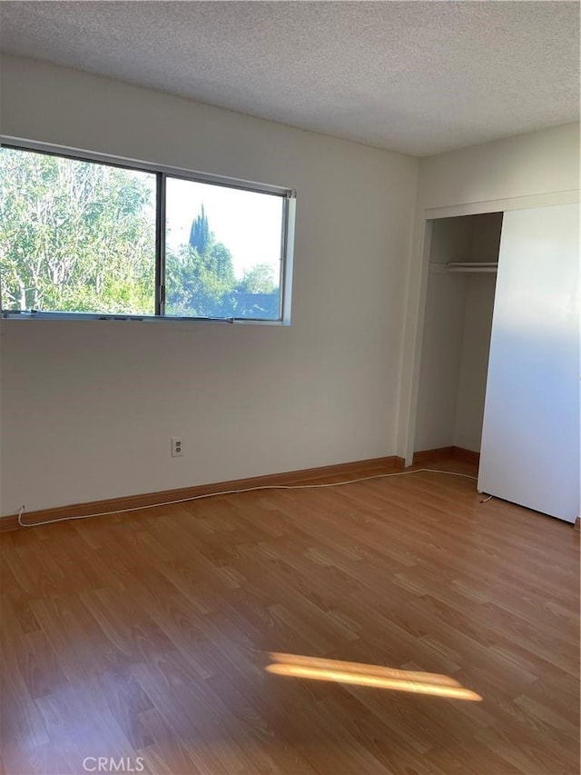 unfurnished bedroom with light wood finished floors, a closet, a textured ceiling, and baseboards