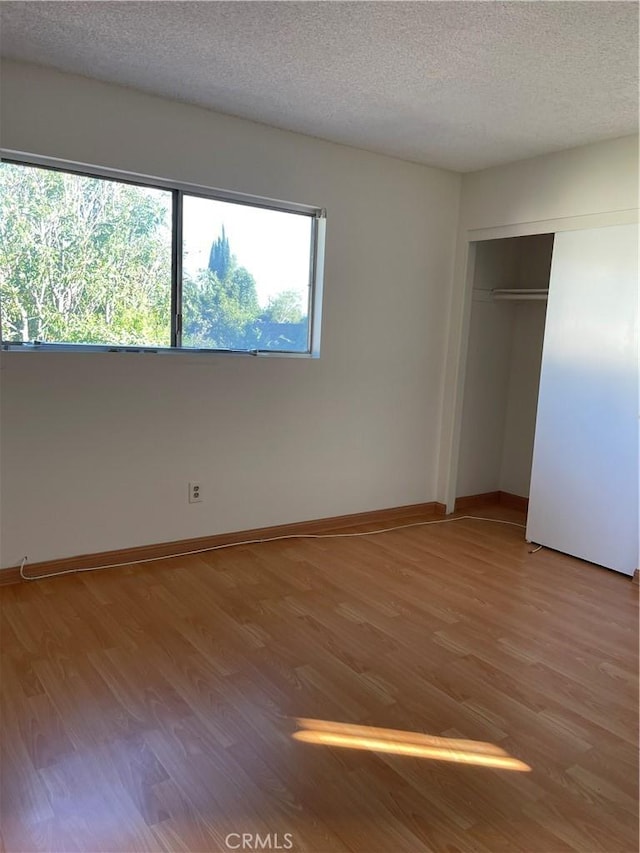 unfurnished bedroom with light wood-style flooring, baseboards, a closet, and a textured ceiling