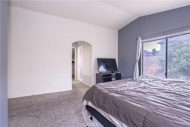 bedroom with vaulted ceiling, carpet flooring, and arched walkways