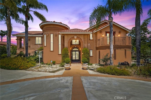 mediterranean / spanish home featuring french doors, a balcony, a tile roof, and stucco siding