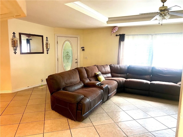 living area featuring ornamental molding, a tray ceiling, light tile patterned flooring, baseboards, and ceiling fan