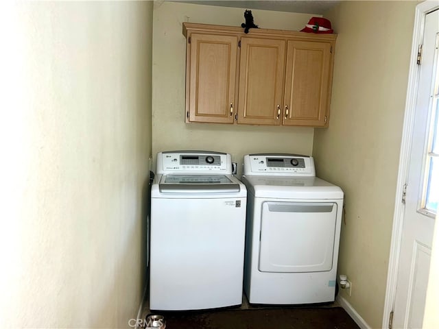 clothes washing area with washer and clothes dryer, cabinet space, and baseboards