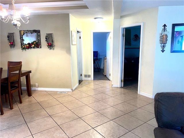 hallway with a notable chandelier, light tile patterned flooring, visible vents, and baseboards