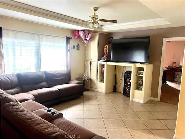 living area with a raised ceiling, a ceiling fan, crown molding, light tile patterned floors, and baseboards