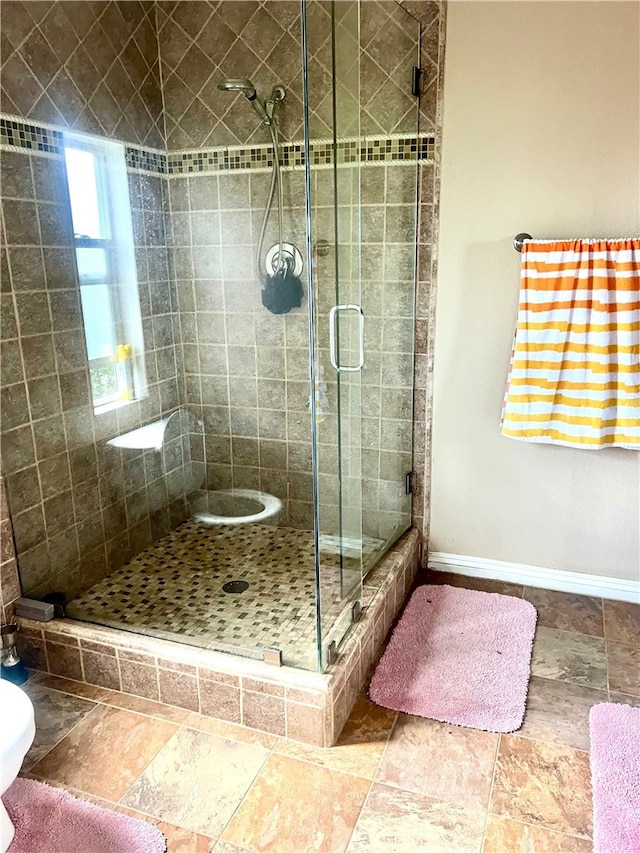 full bath featuring baseboards, a stall shower, and stone finish floor