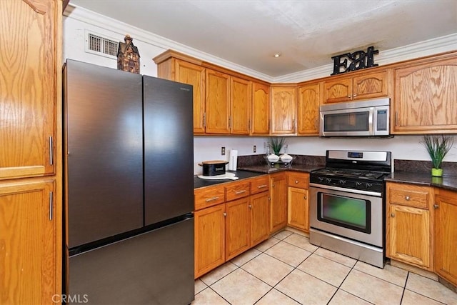 kitchen with dark countertops, ornamental molding, light tile patterned floors, and stainless steel appliances