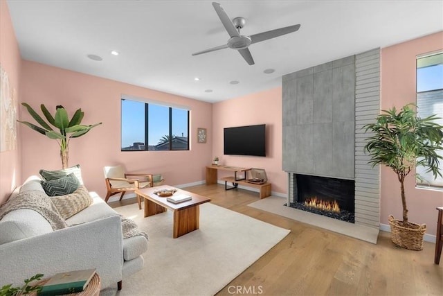 living area with a wealth of natural light, light wood-type flooring, a large fireplace, and ceiling fan