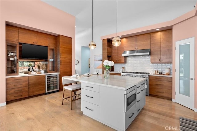 kitchen with decorative backsplash, wine cooler, appliances with stainless steel finishes, under cabinet range hood, and brown cabinets