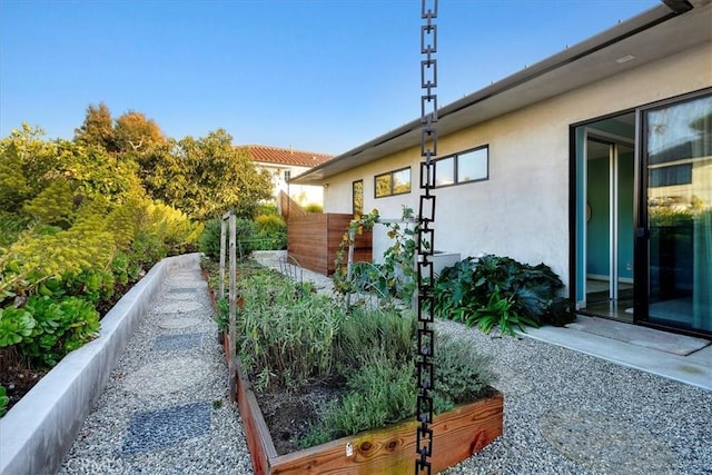 view of side of home featuring a vegetable garden, fence, and stucco siding