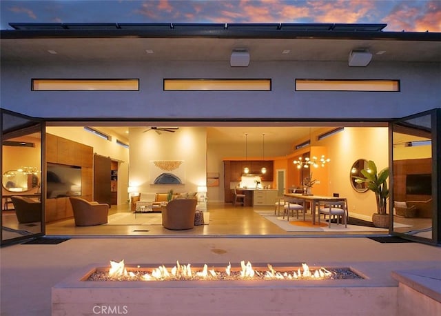 back of property at dusk with an outdoor living space with a fire pit, a patio, a ceiling fan, and stucco siding