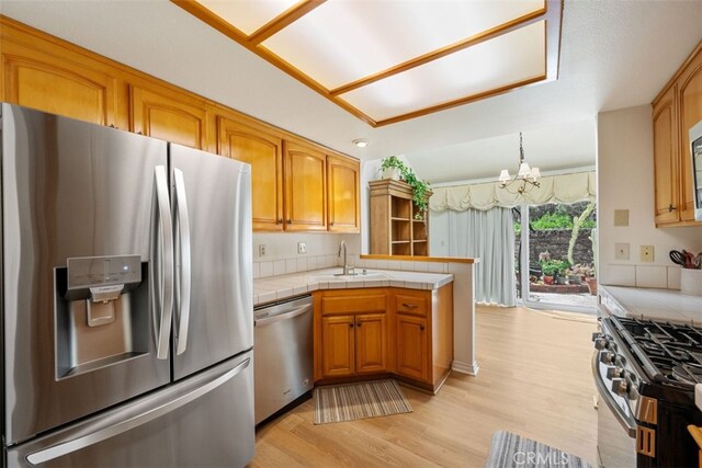 kitchen with light wood finished floors, a sink, tile counters, appliances with stainless steel finishes, and a chandelier