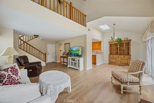 living area featuring stairway, baseboards, high vaulted ceiling, a skylight, and light wood-type flooring