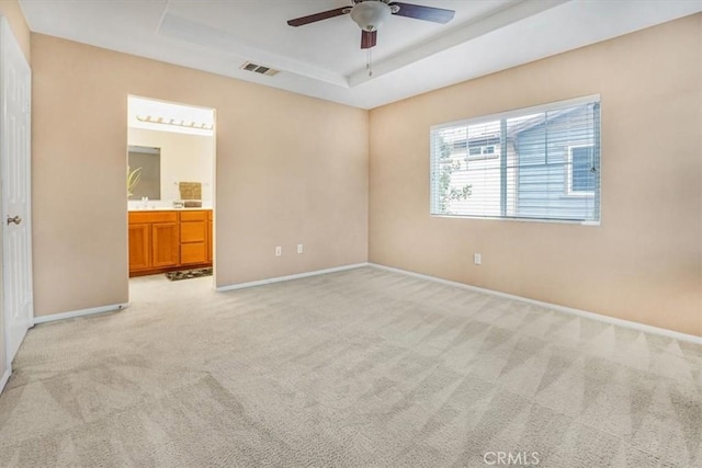 unfurnished bedroom featuring visible vents, connected bathroom, baseboards, light colored carpet, and a tray ceiling