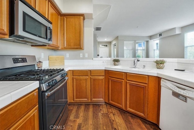 kitchen featuring visible vents, brown cabinets, appliances with stainless steel finishes, dark wood-style floors, and a sink