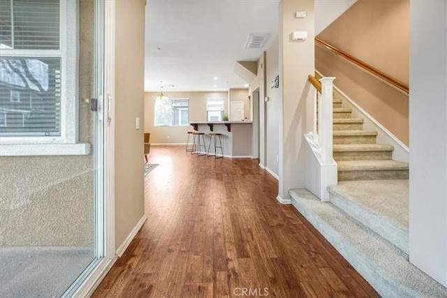 corridor with stairway, wood finished floors, visible vents, and baseboards