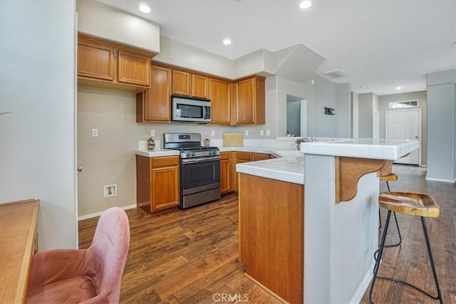 kitchen featuring brown cabinets, a peninsula, stainless steel appliances, and dark wood-type flooring