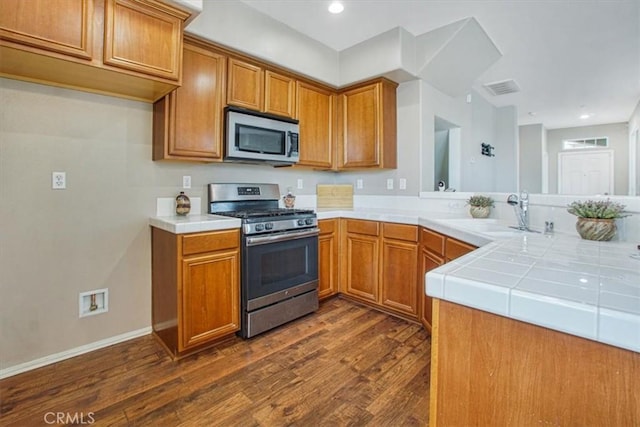 kitchen with brown cabinetry, visible vents, dark wood-style flooring, a sink, and stainless steel appliances