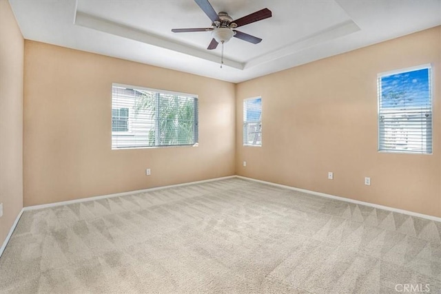 carpeted spare room with baseboards, a raised ceiling, and a ceiling fan