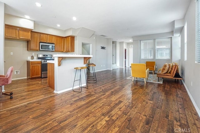 kitchen with a kitchen bar, brown cabinets, stainless steel appliances, light countertops, and dark wood-style flooring