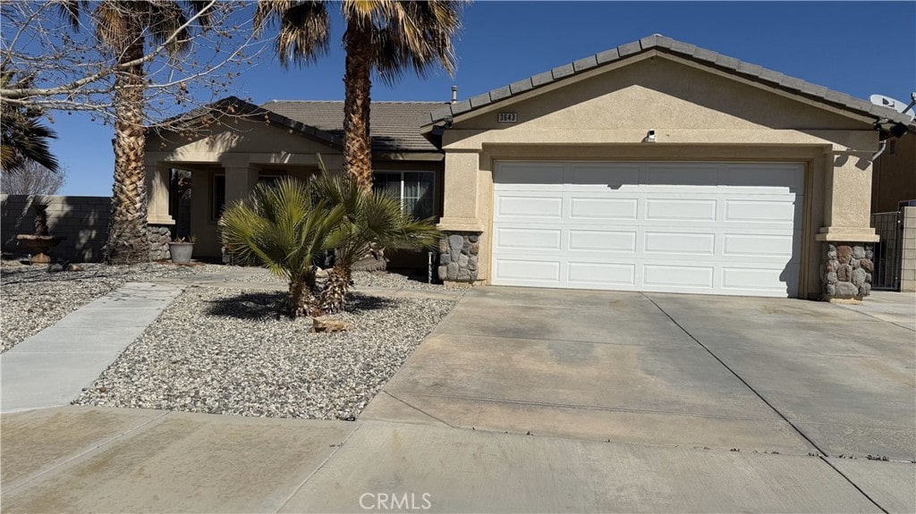 single story home with stucco siding, stone siding, a garage, and driveway