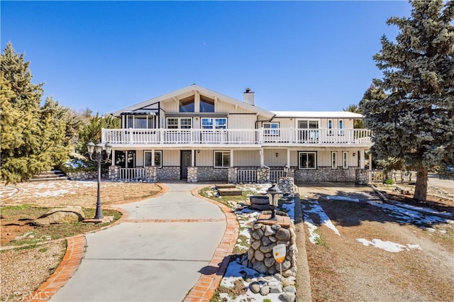 view of front of property featuring a balcony, stone siding, and a chimney