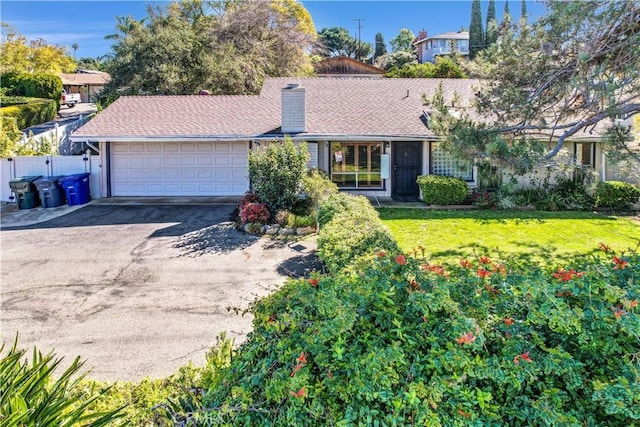 ranch-style house with an attached garage, fence, a front yard, a chimney, and driveway