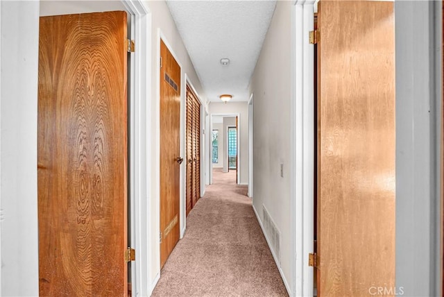 hallway with visible vents, carpet floors, a textured ceiling, and baseboards