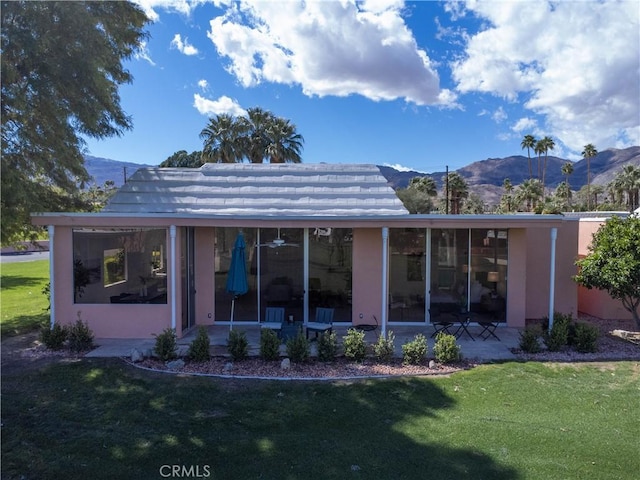 back of property with a mountain view, a lawn, stucco siding, and a sunroom