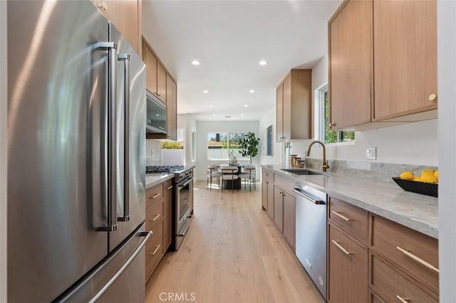 kitchen with light stone countertops, light wood finished floors, recessed lighting, a sink, and premium appliances