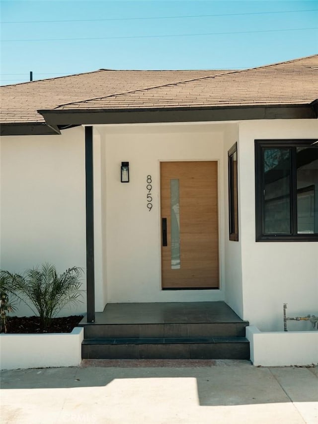 doorway to property featuring roof with shingles and stucco siding