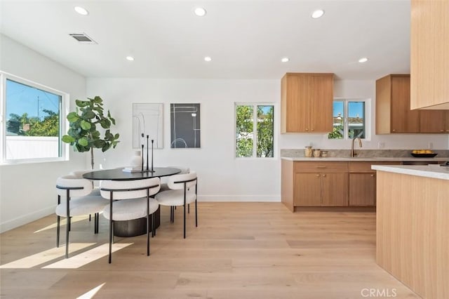 kitchen with baseboards, light countertops, recessed lighting, light wood-style floors, and a sink