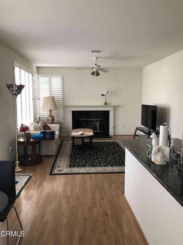 living room with a glass covered fireplace, wood finished floors, visible vents, and ceiling fan