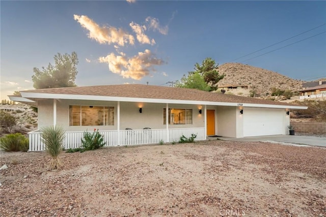 ranch-style house with a porch, an attached garage, driveway, and stucco siding